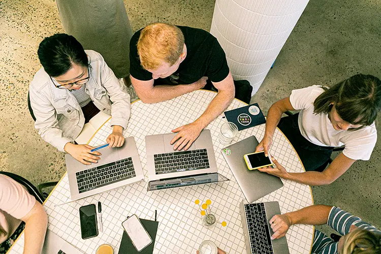 Grupo de estudiantes colaborando en un ambiente de trabajo en equipo en una mesa de oficina moderna.