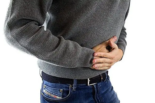 Dolor abdominal y molestias estomacales en persona con sudadera gris y jeans, sensación de incomodidad en el área del abdomen.